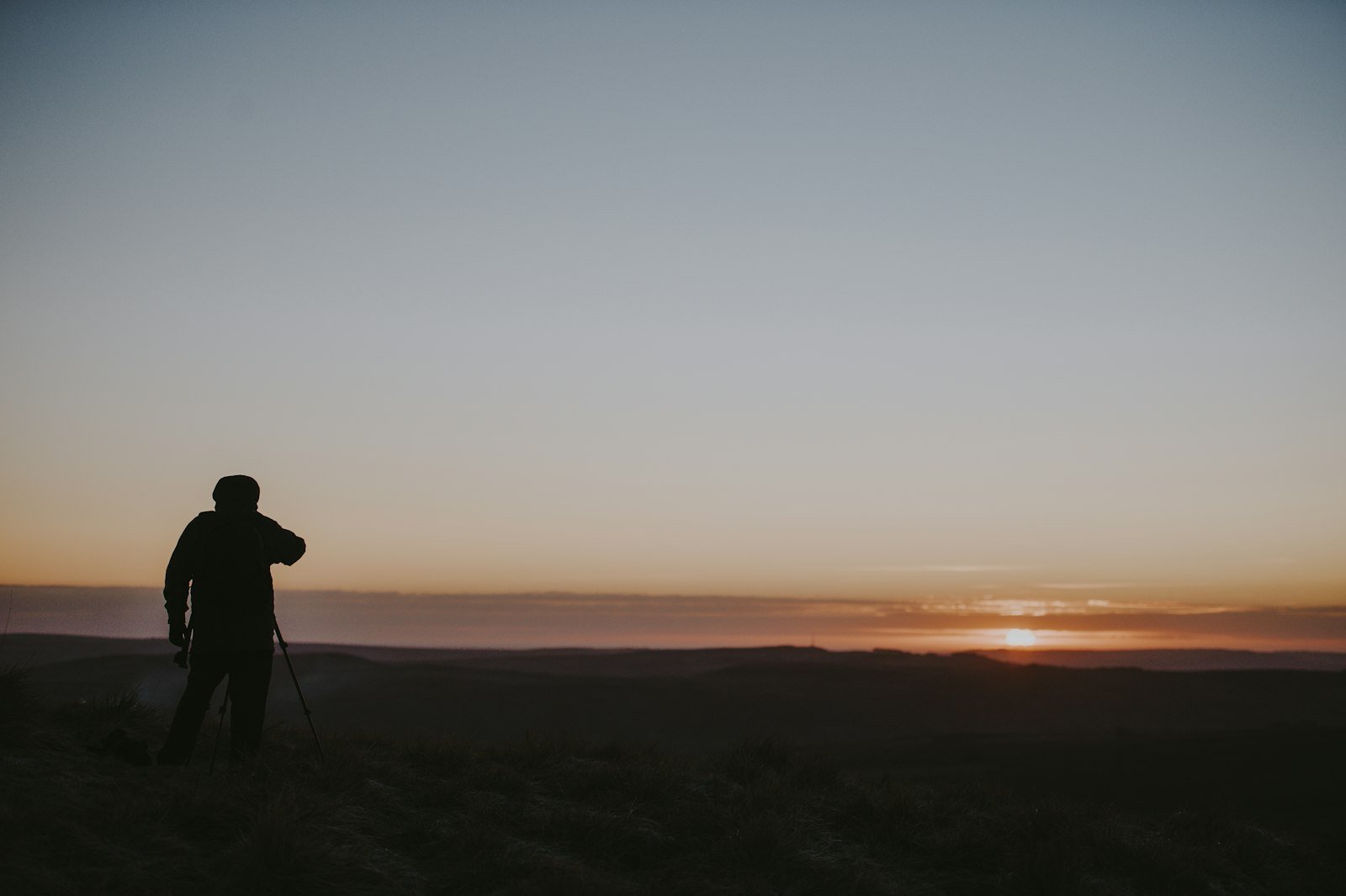 A solitary figure stands at a hilltop overlook at sunrise, gazing across a valley in quiet, hopeful reflection.