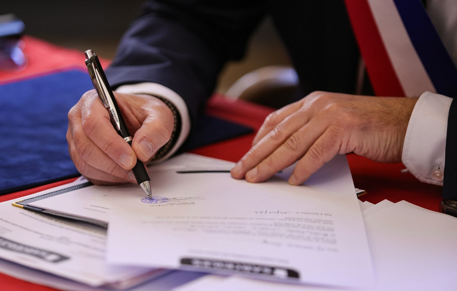 A person carefully reviews and signs a legal document with a pen at a wooden desk, conveying focused preparation.